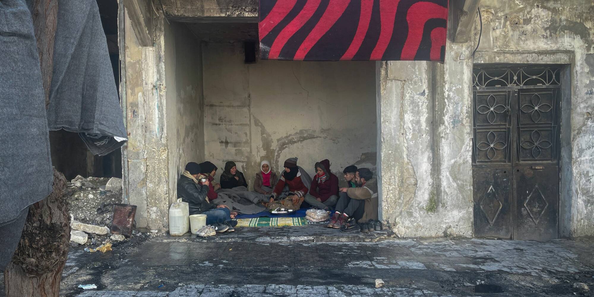Eine Gruppe von Menschen sitzt zusammen in einem zerstörten Gebäude